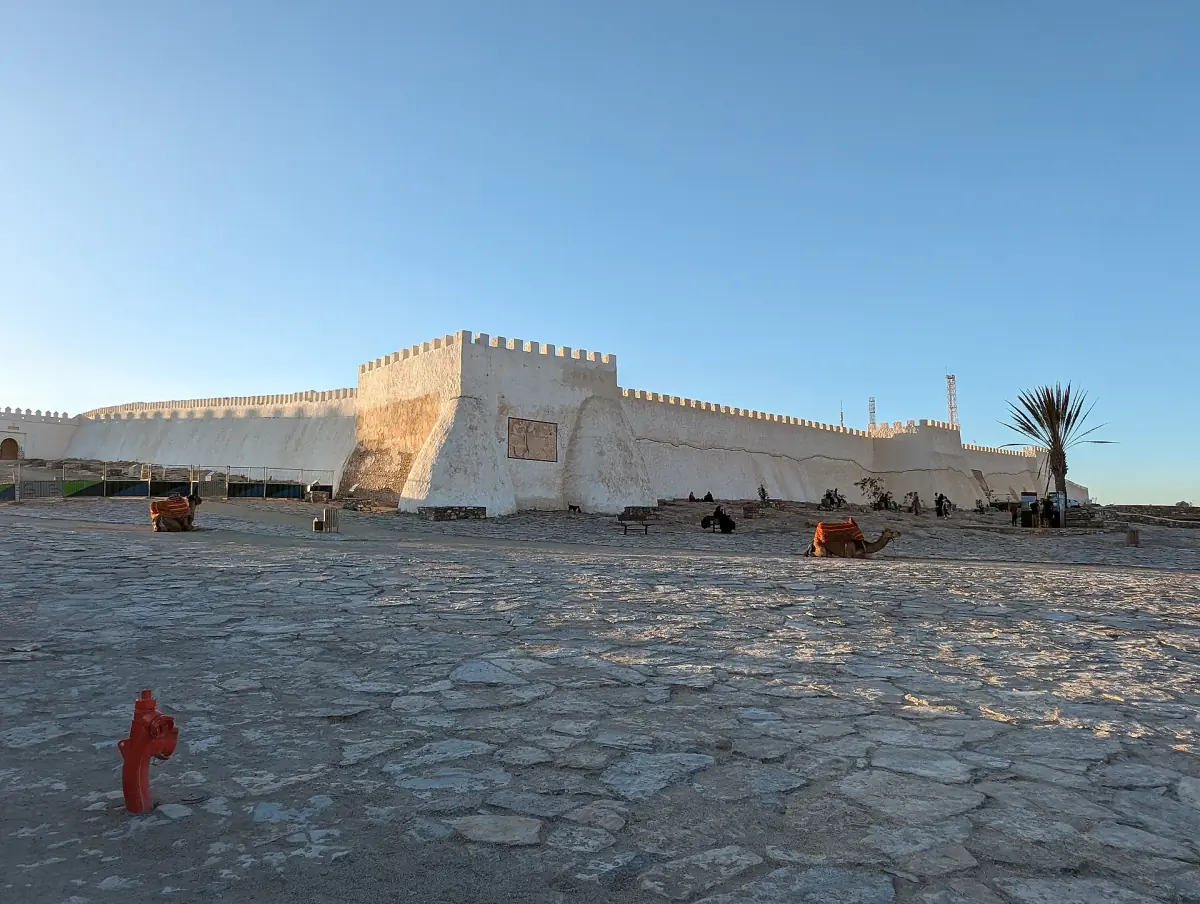 Crenellated white wall of the Agadir Oufella kasbah above a paved square with a palm