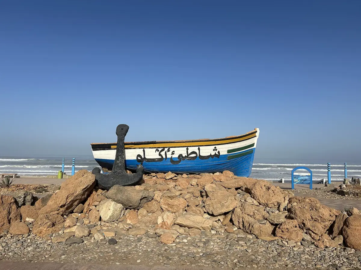 Blue and white fishing boat displayed on rocks with an anchor beside Aglou beach