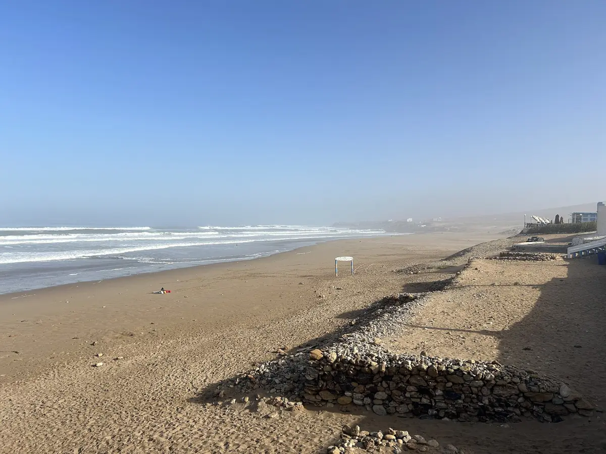 Long empty beach at Aglou with waves rolling in and a promenade beside it