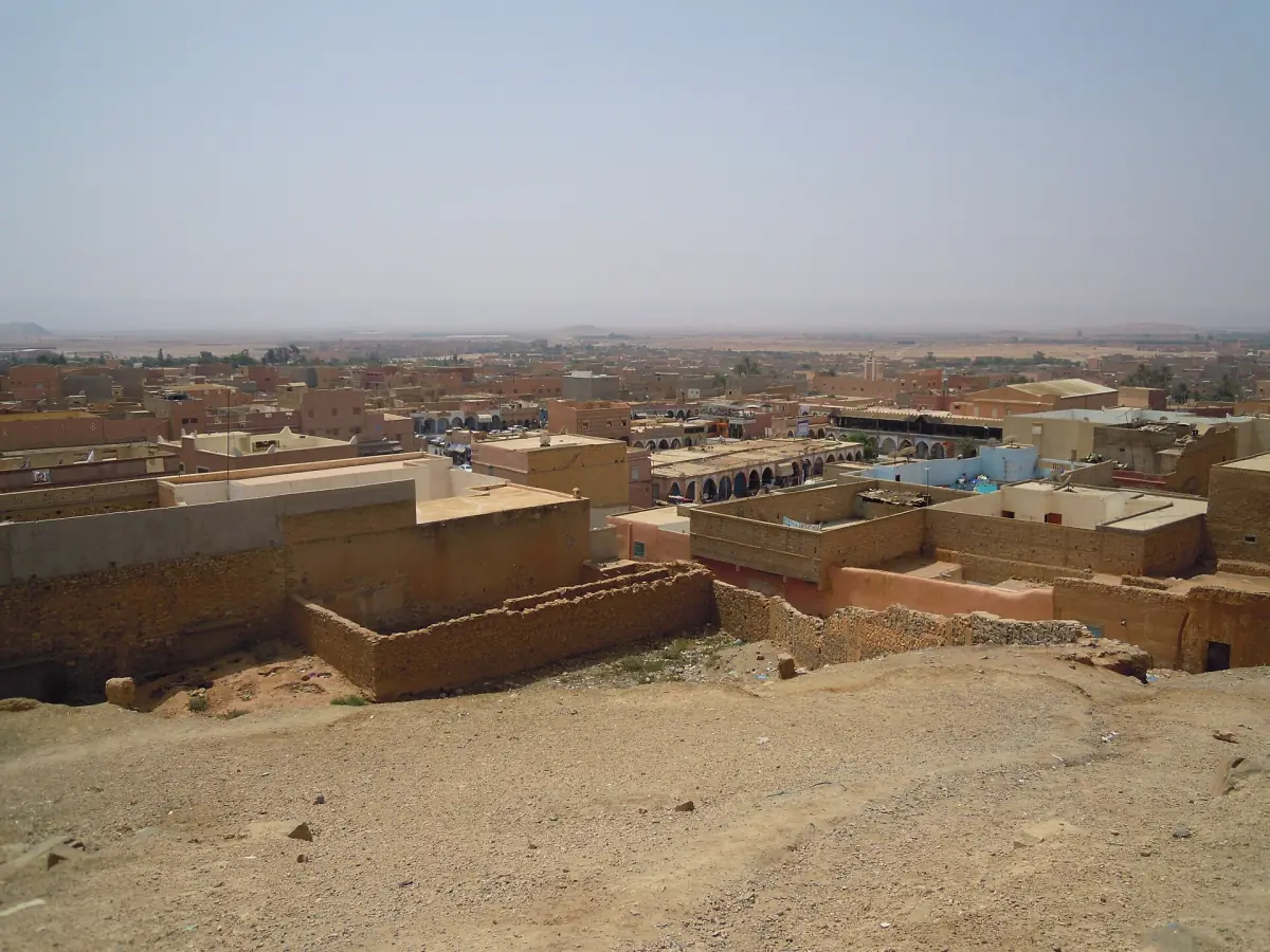 View over Guelmim's flat-roofed mud-brick houses from a dry hillside in hazy light