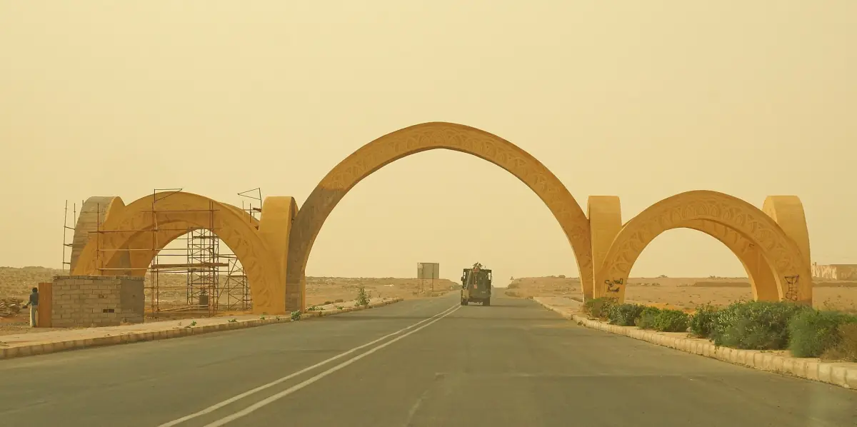 Large sandy-coloured arched city gate over the road at the western entrance of Guelmim