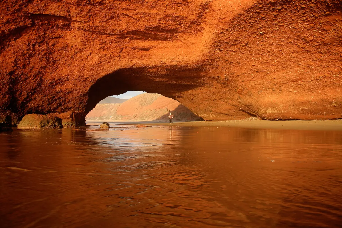Orange-lit Legzira arch reflected in shallow water on the wet sand