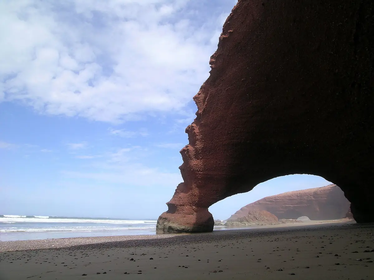Red sandstone arch of Legzira beach rising from the sand under a blue sky