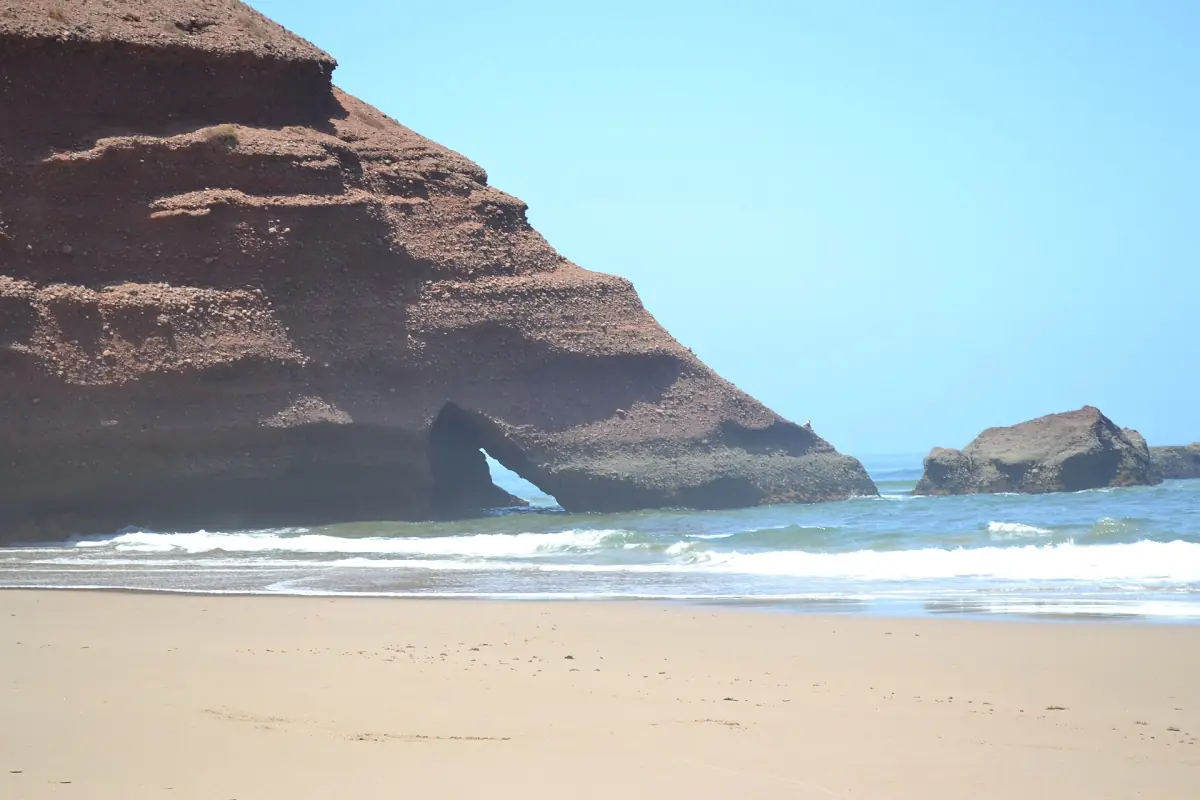 Legzira rock arch above a sandy beach with turquoise surf in clear weather