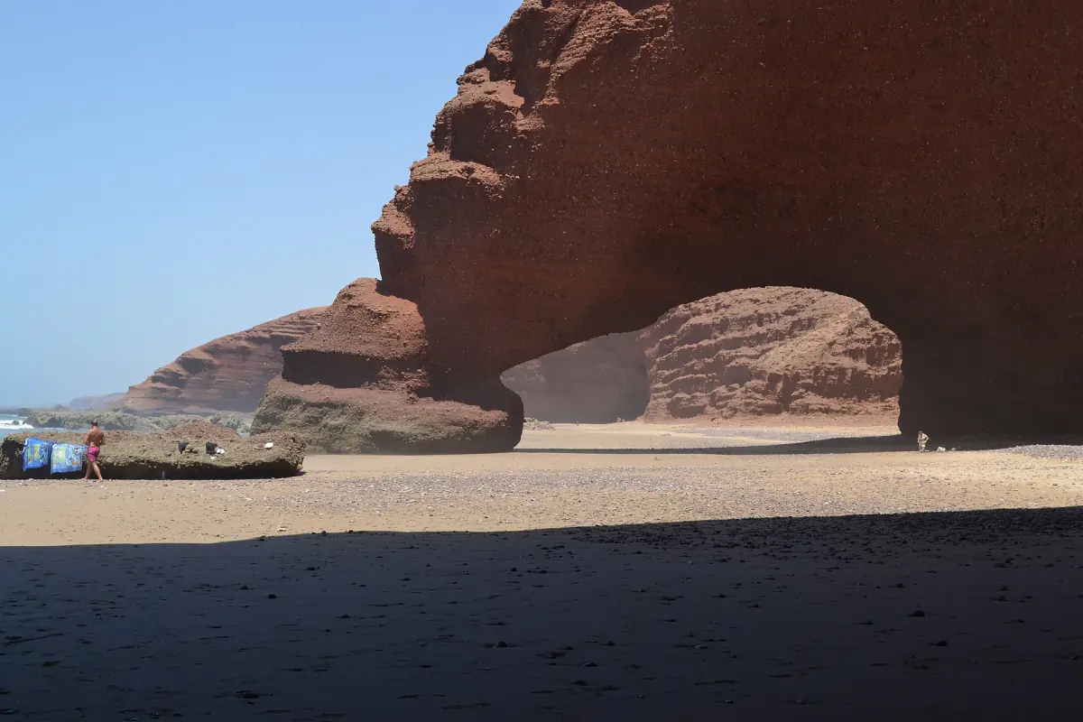 Red cliffs and arch of Legzira at low tide with pebbles and sand in front