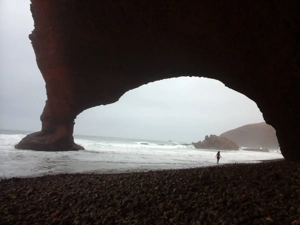 View from under the Legzira arch towards the sea with a lone walker on the shore