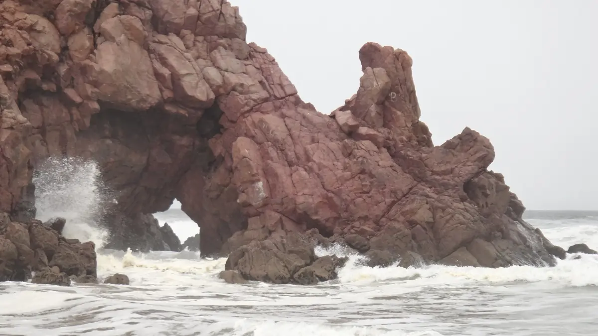 Red rock formation with a natural sea arch and a wave splashing near Mirleft