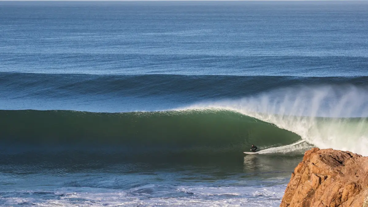 Surfer riding a green barrel wave beside a rocky point on the Atlantic coast