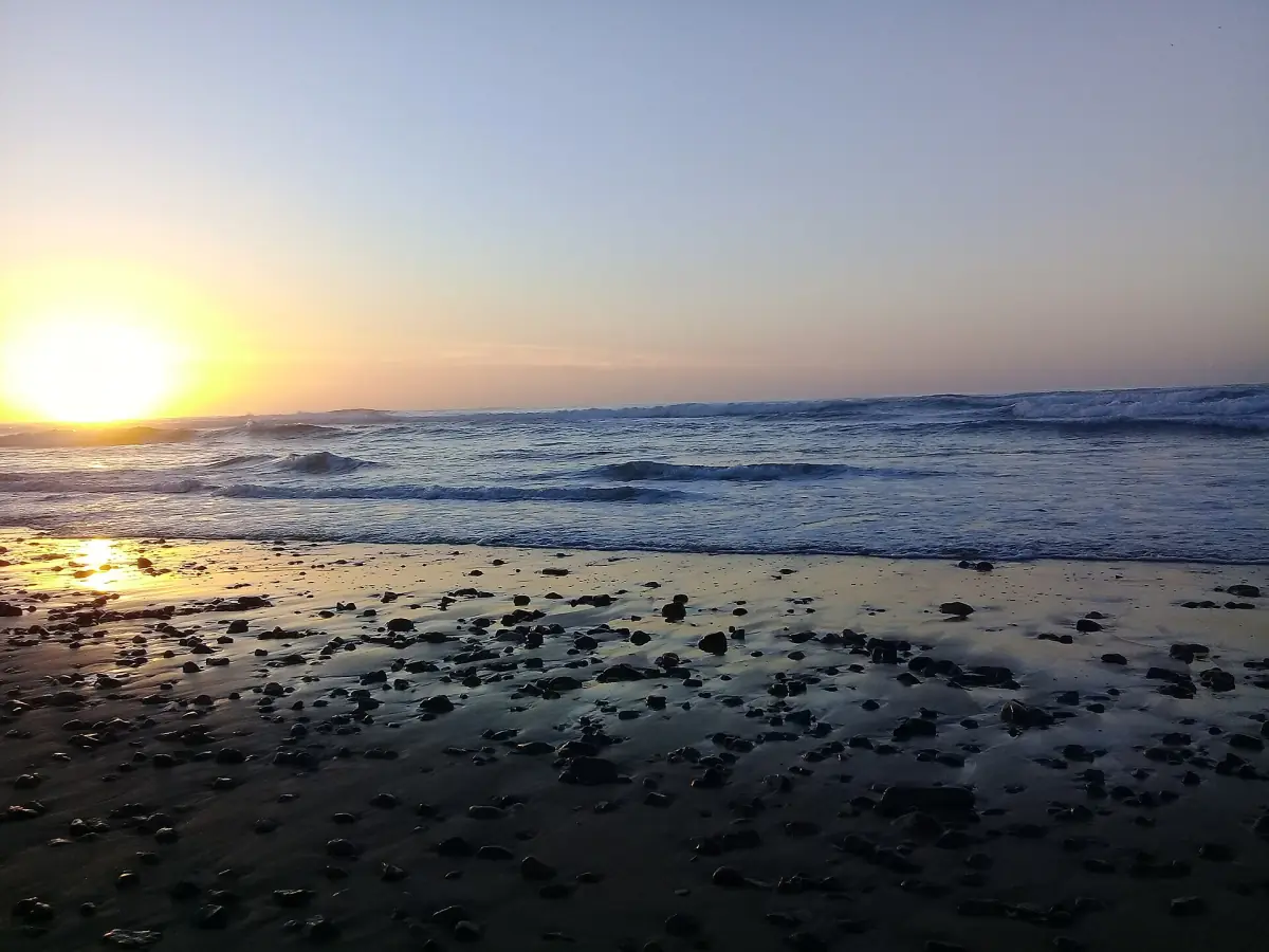 Sun setting over wet sand and dark rocks on the beach at Sidi Ifni