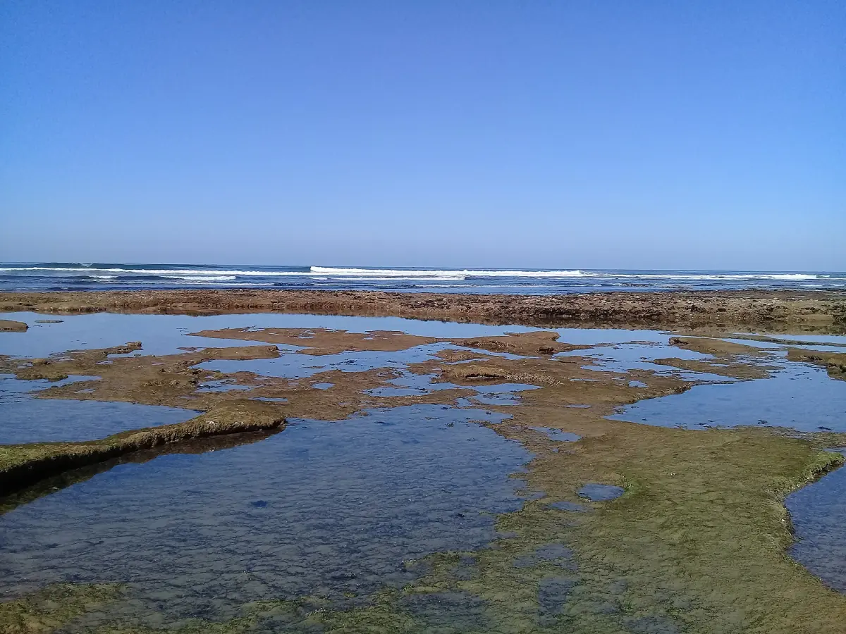 Shallow rock pools and waves on the flat rocky shore near Sidi Ifni at low tide
