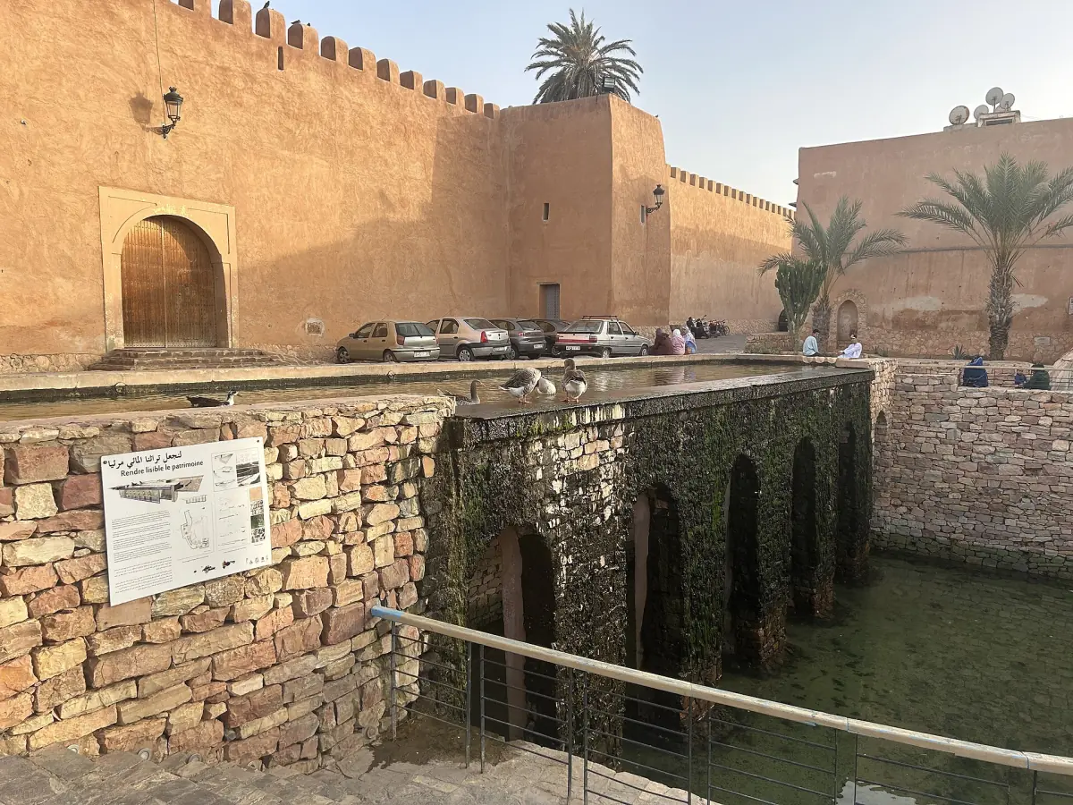 Ochre rampart walls and arched gate of Kasbah Aghnaj in Tiznit beside a stone channel